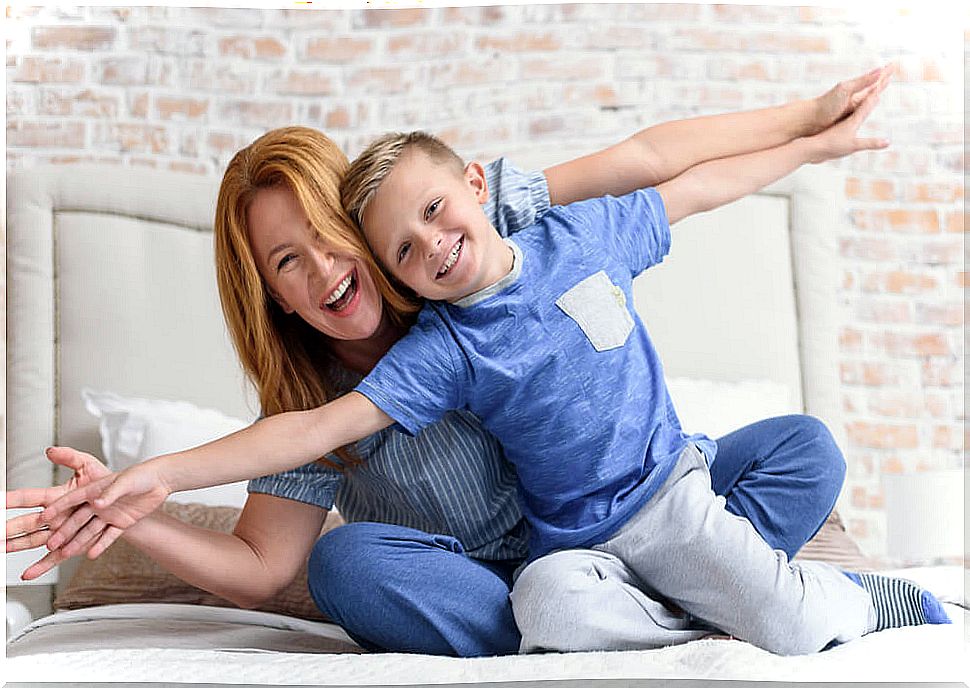 Mother of more than 35 years and her son of 8 laughing on the bed with outstretched arms