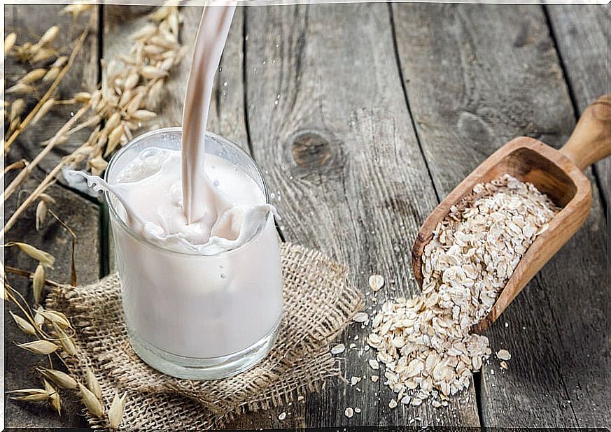 Oat grains in a wooden spoon and a glass with oatmeal drink