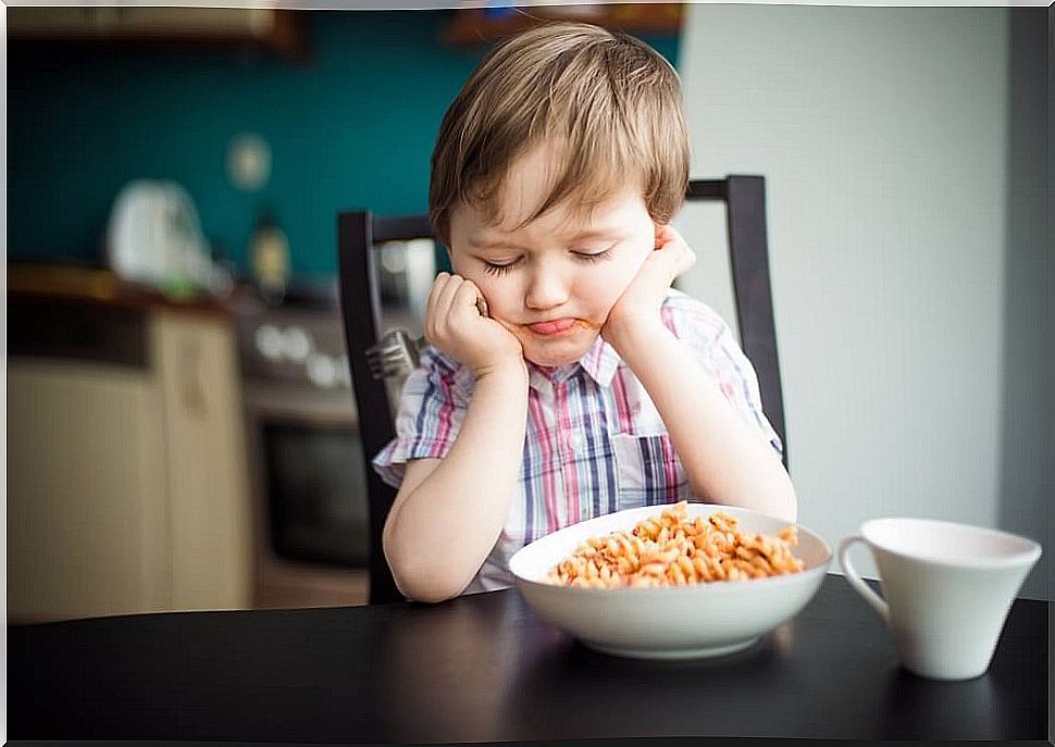 Boy sitting in front of a plate of food angry.